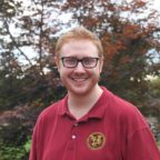 Ben smiling wearing red polo shirt with trees in background