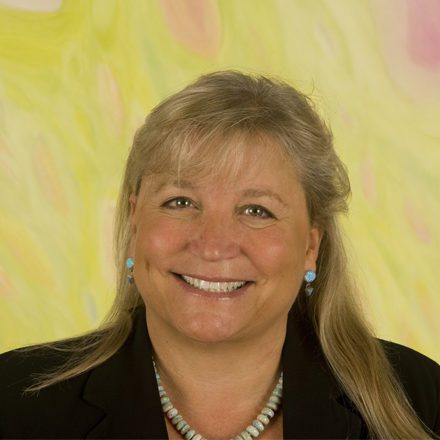 Linda smiling wearing earrings and necklace with black suit jacket