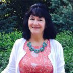 Loretta smiling outside wearing coral shirt and white sweater