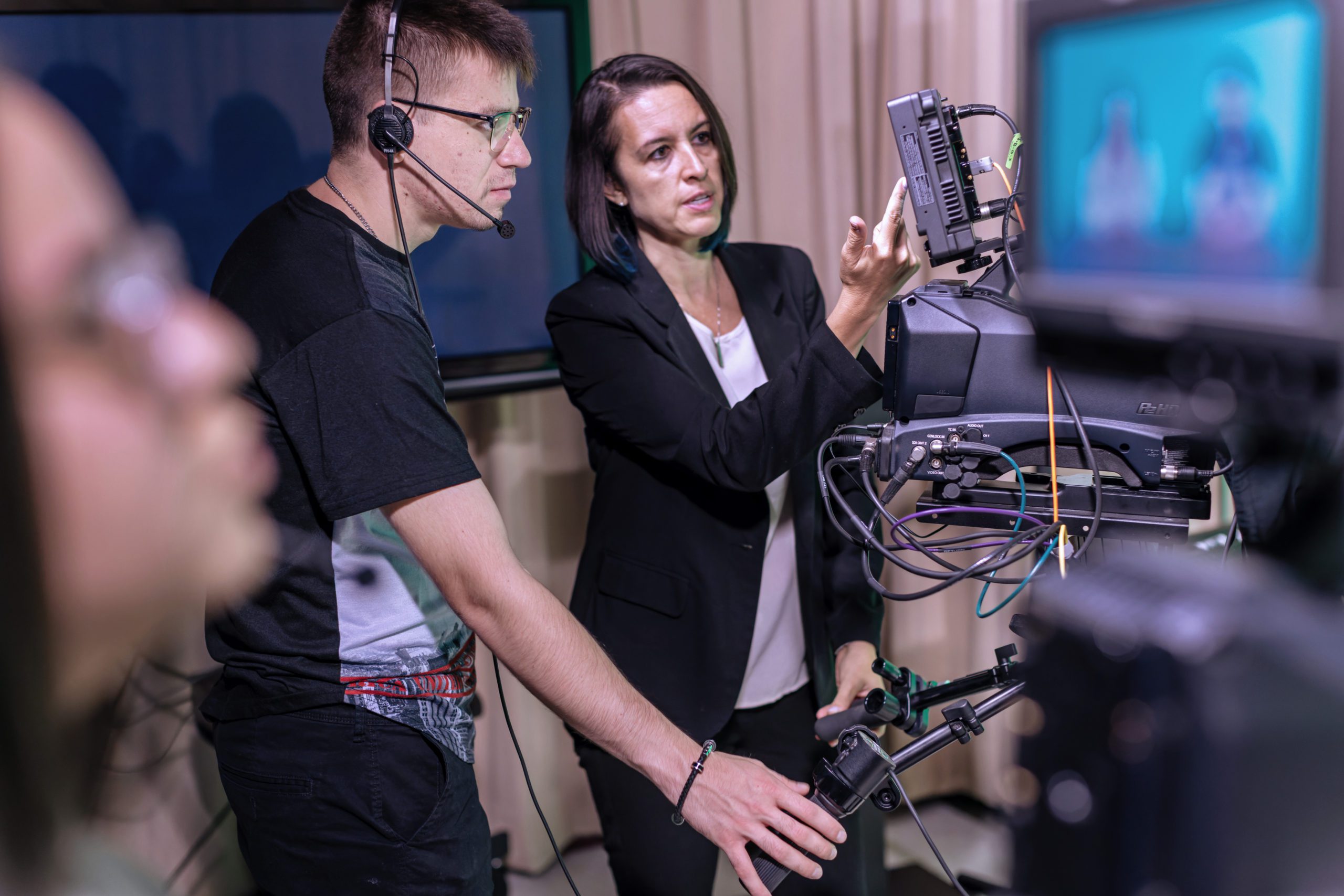 A male student with headphones on working with a camera with his professor.