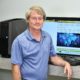 Dr. Vermilyer smiling wearing blue dress shirt next to computer in classroom