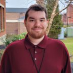 William smiling outside wearing maroon shirt and black lanyard for id card