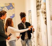 Three students looking at an art on the wall.