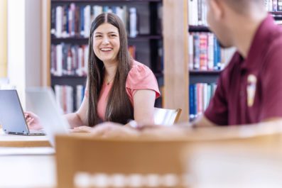 A male and female student sitting at desks in the library.