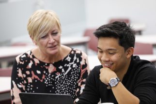 A student and a professor sitting at a desk and working on a computer.