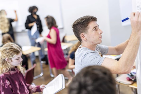 Students in a classroom writing on white boards.