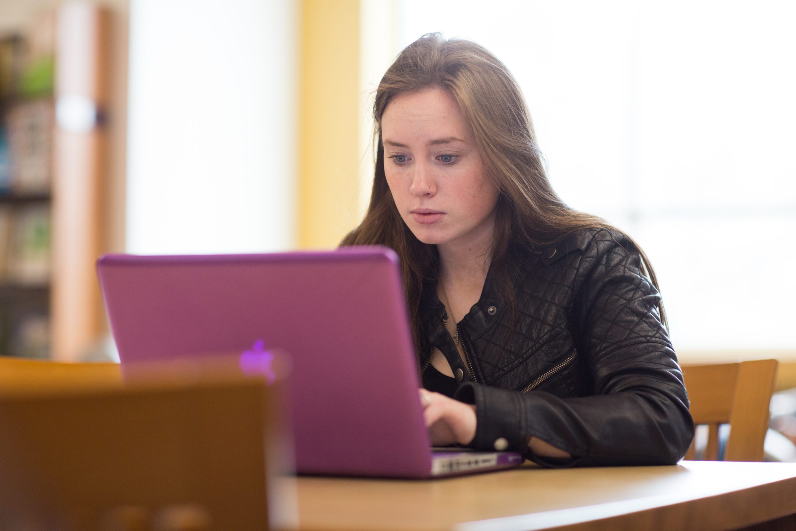 A female student sitting at a table in the library with her laptop on the table in front of her.