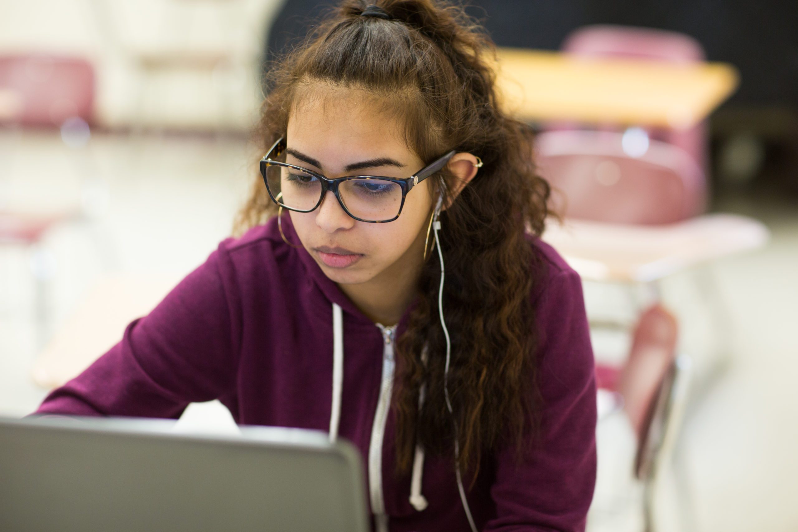 A female student sitting at a desk in a classroom with a computer in front of her.