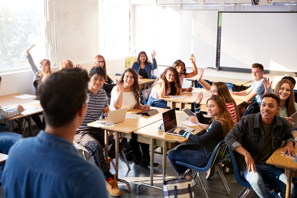 Students sitting at desks in a classroom and raising their hands