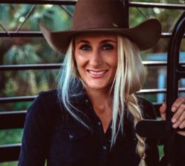 Jayden wearing hat and black long sleeve shirt with blonde hair in a braid smiling
