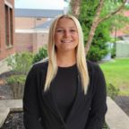 Victoria smiling outside of Borelli Hall wearing black shirt and blazer jacket