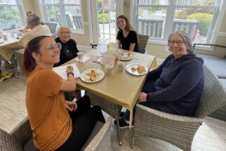 two students and two participants at assisted living center seated at table smiling enjoying food together
