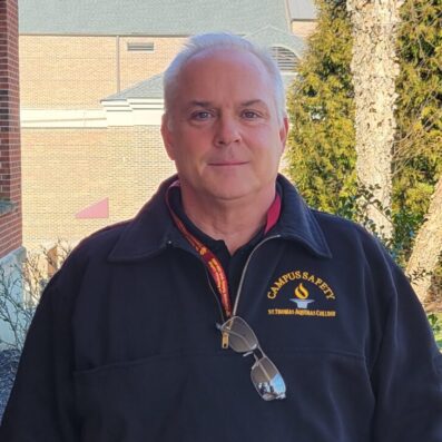 Ken smiling wearing campus safety sweatshirt with trees in background outside