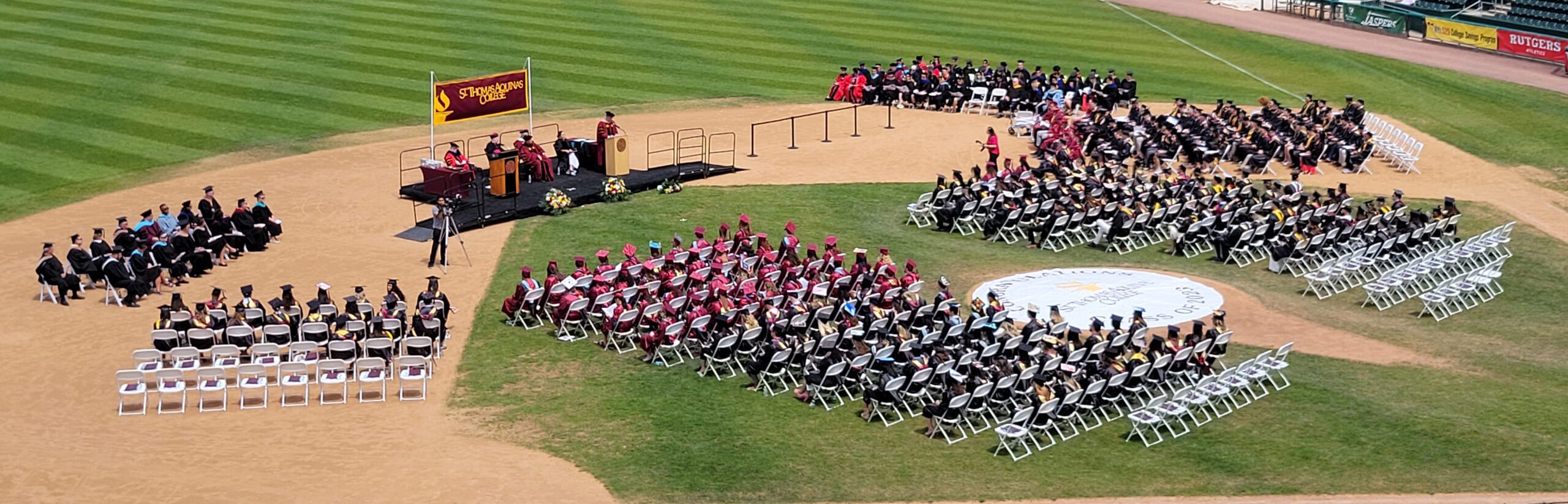 Commencement 2023 image from seats at Clover stadium while graduates are on the field in regalia walking across stage