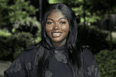 Fatima smiling wearing black sweatshirt with green trees in background