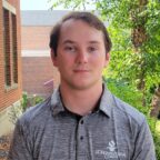 Brad outside smiling wearing gray residence life shirt