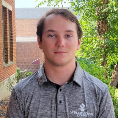 Brad outside smiling wearing gray residence life shirt