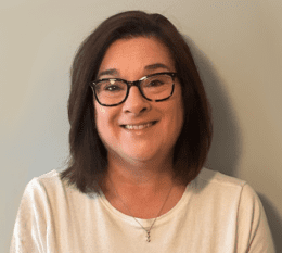 Lisa Horgan smiling wearing black rimmed glasses and cream colored shirt with drop necklace