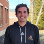 Nicholas smiling outside of Borelli Hall wearing STAC Volleyball black sweatshirt