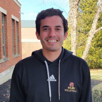 Nicholas smiling outside of Borelli Hall wearing STAC Volleyball black sweatshirt