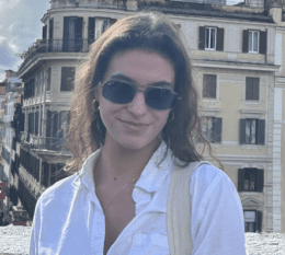 Sydney smiling wearing sunglasses with buildings and city streets of Rome in background