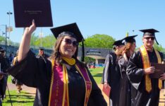 student after ceremony holding up diploma case smiling