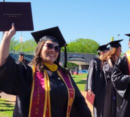 student after ceremony holding up diploma case smiling