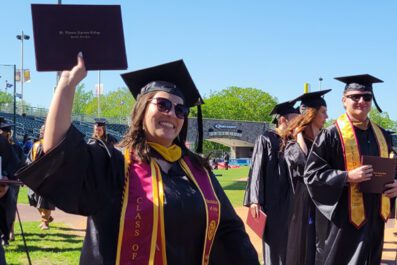 student after ceremony holding up diploma case smiling