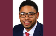 Kameron smiling wearing suit jacket red tie and black rimmed glasses