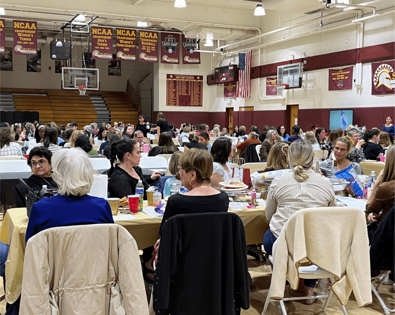 Aquinas Hall Gymnasium showing many tables with people seated in chairs, talking to each other.