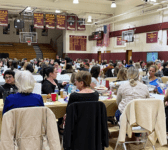 Aquinas Hall Gymnasium showing many tables with people seated in chairs, talking to each other.
