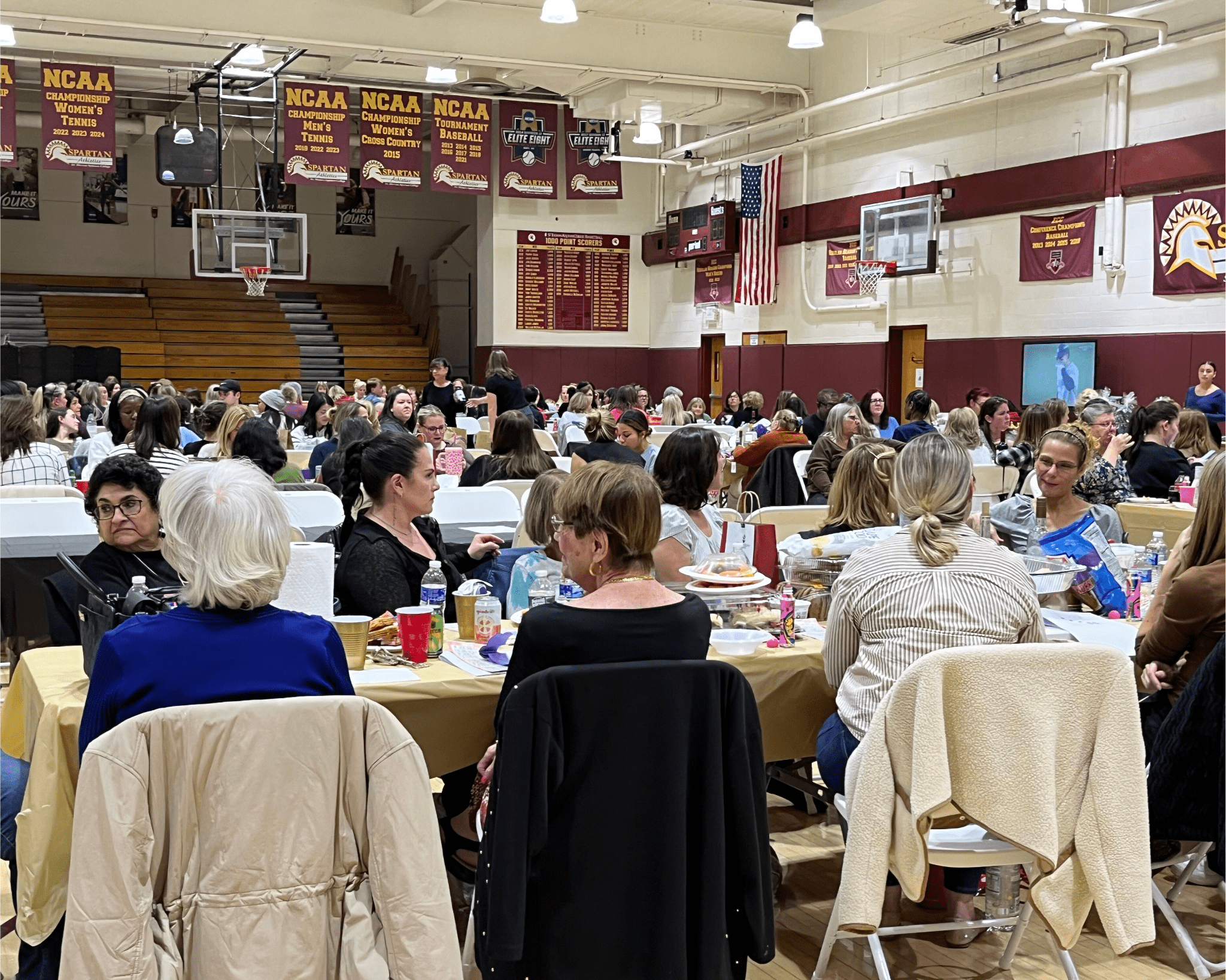 Aquinas Hall Gymnasium showing many tables with people seated in chairs, talking to each other.