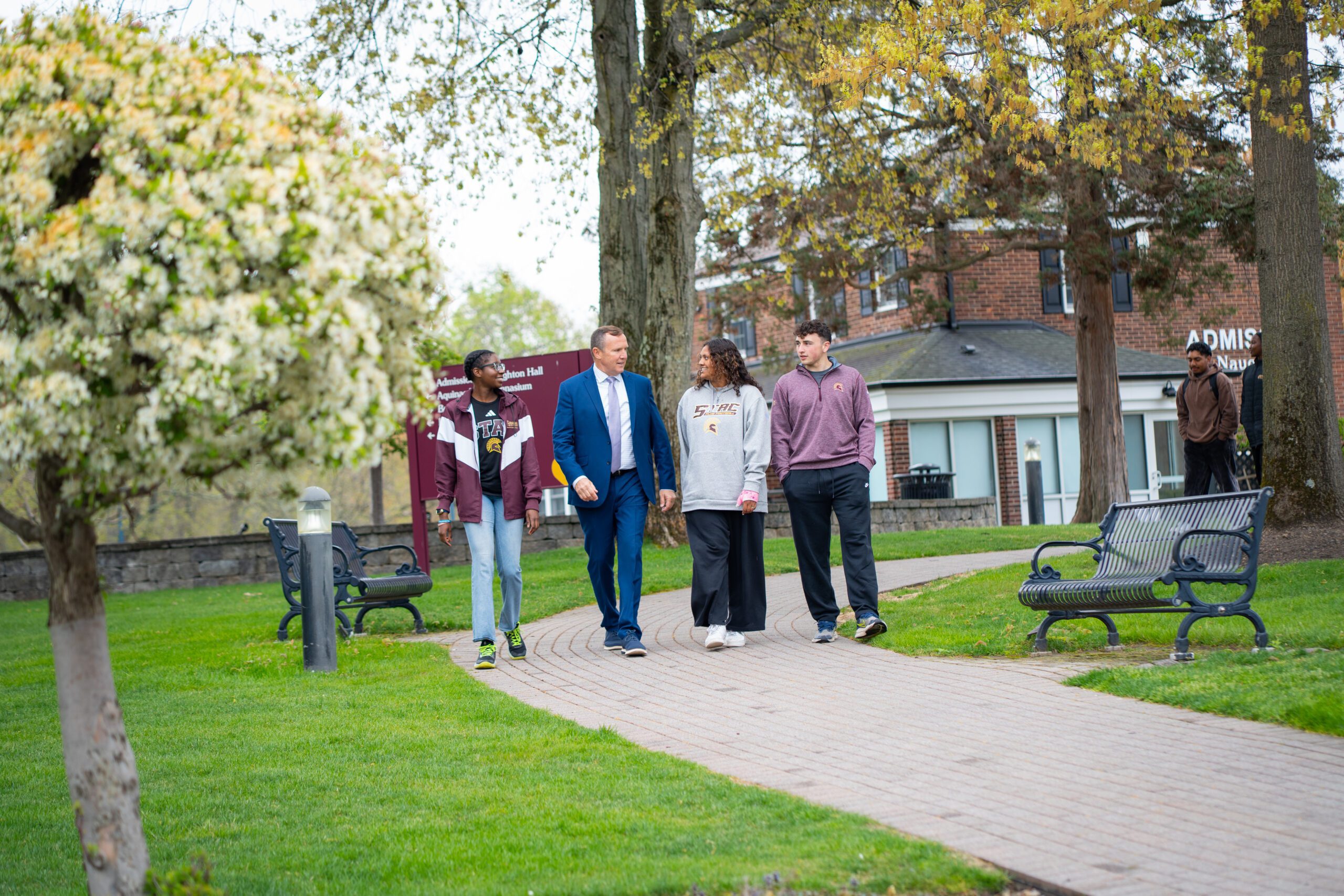 President Daly walking outside of Admissions office with three students